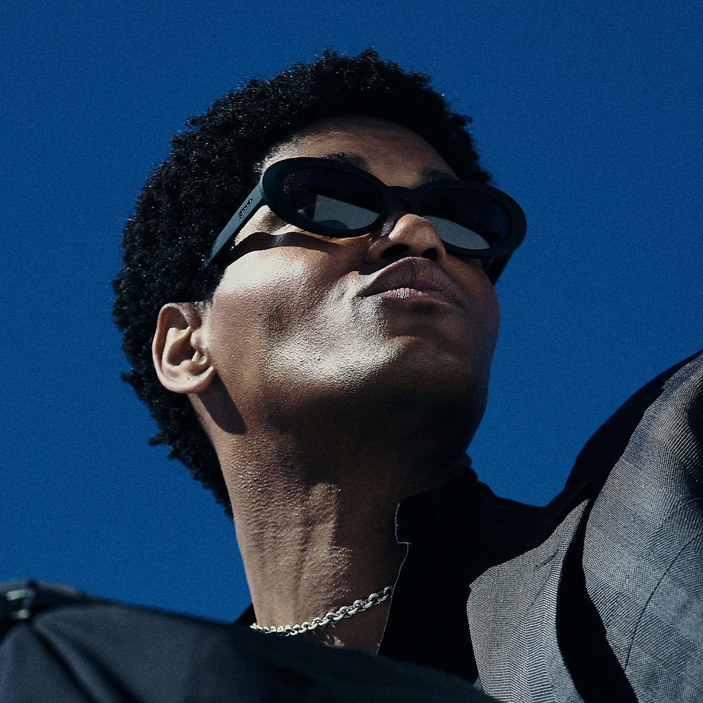 Low-angle view of a man wearing black oval sunglasses with polarized lenses against a white background.