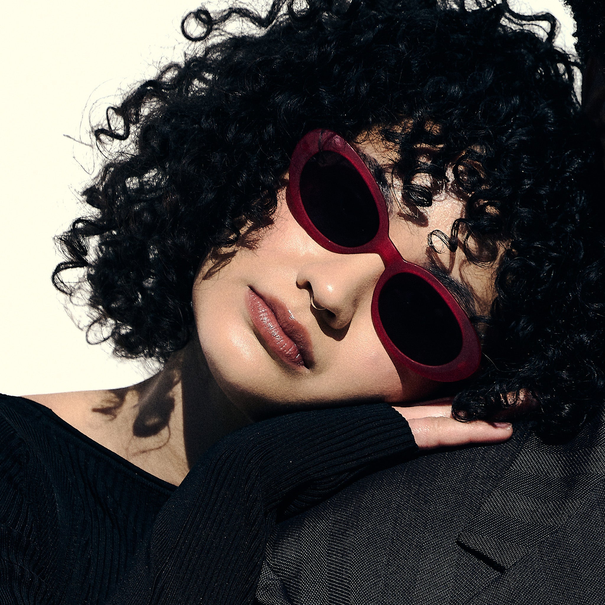 A woman poses while wearing hot pink oval sunglasses with dark red polarized lenses.