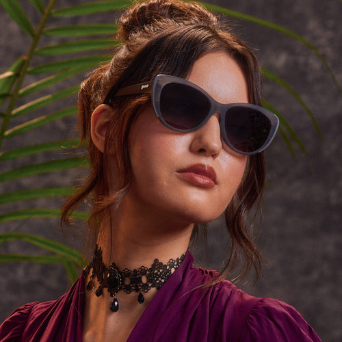 An elegantly dressed woman in translucent gray cat-eye sunglasses with black gradient lenses.
