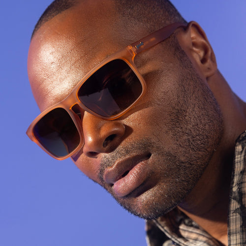 A stylish man with dark cropped hair gives a moody pout to the camera in brown Grand Gs with brown-gray gradient lenses.