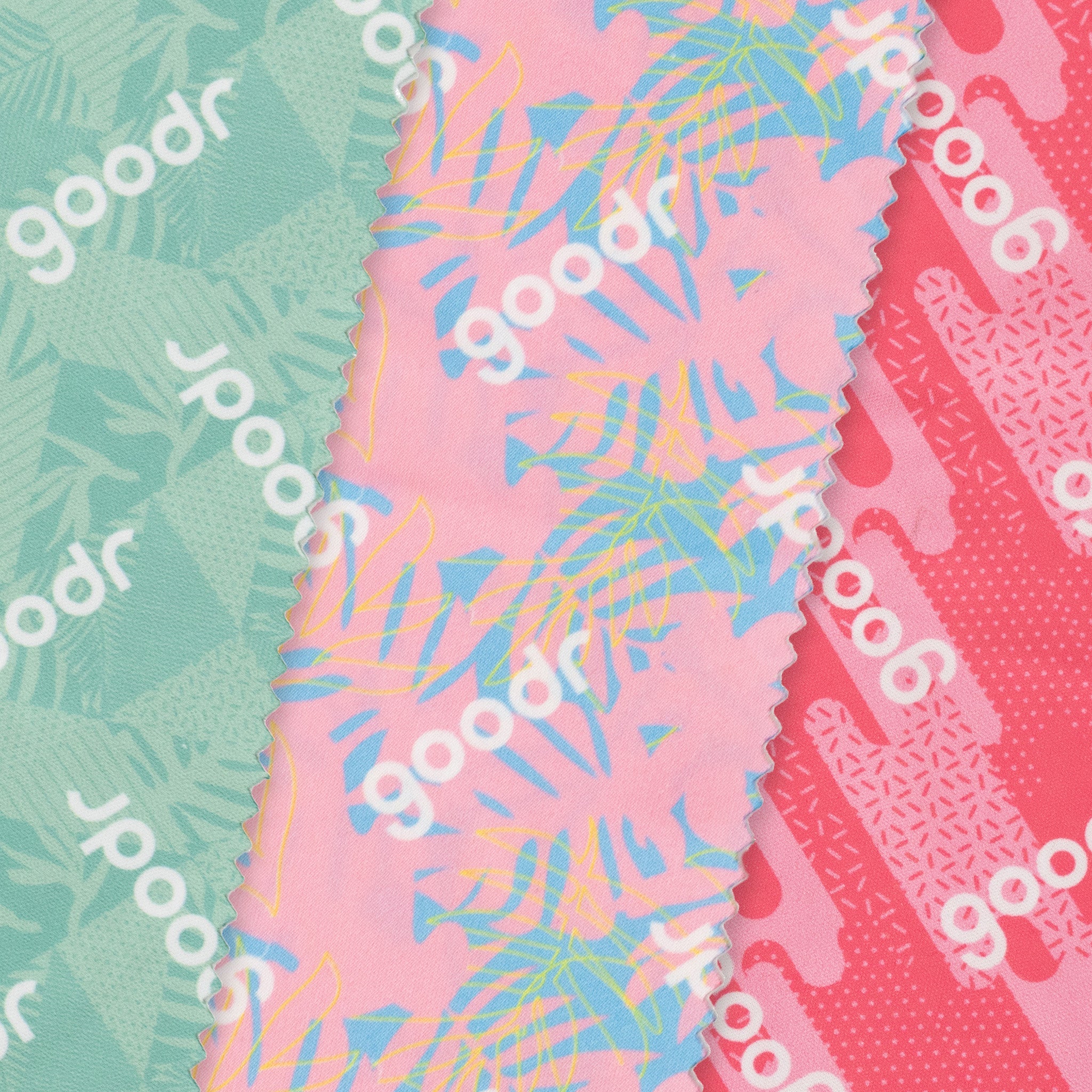 Close-up of three microfiber lens cloths with a geometric tropical print in shades of pink and teal overlapping each other.