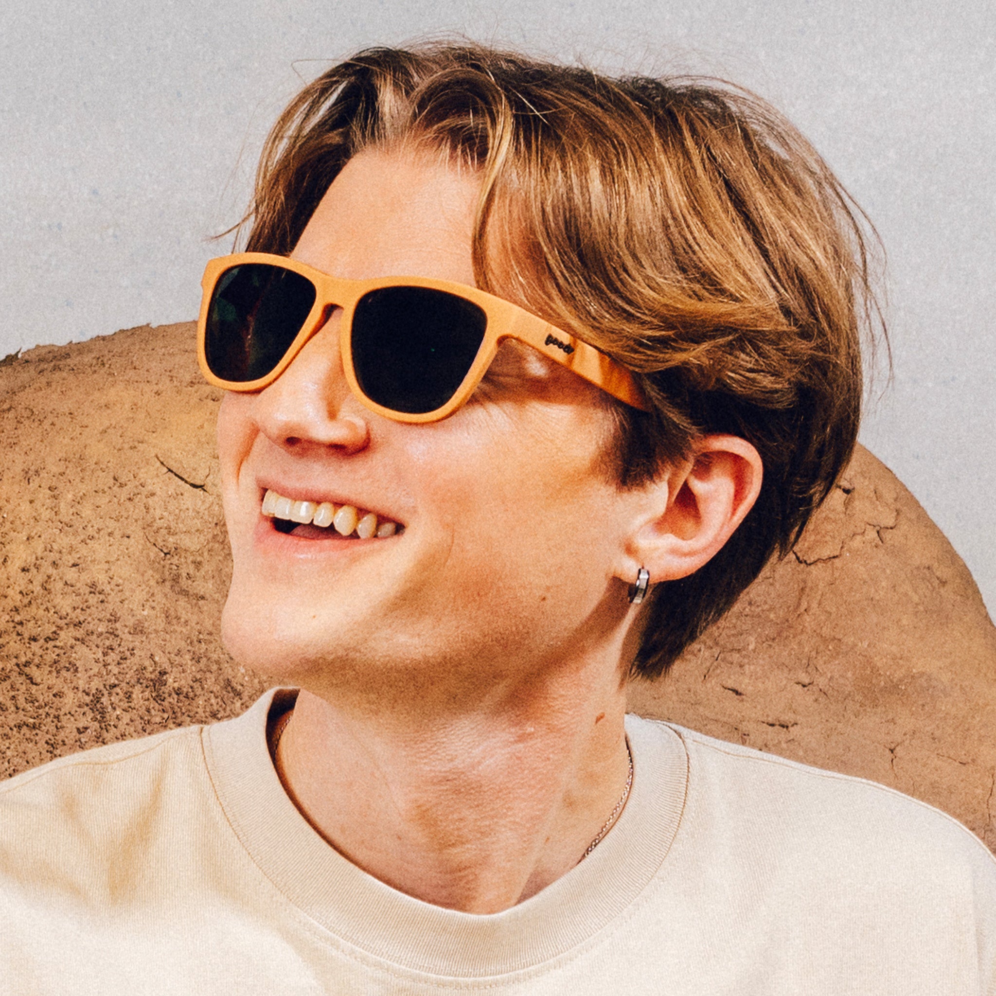 Man wearing classic brown sunglasses with green non-reflective lenses smiles in front of a desert backdrop.